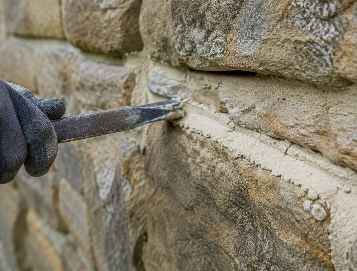 Lime mortar being pressed into a stone joint with a pointing iron